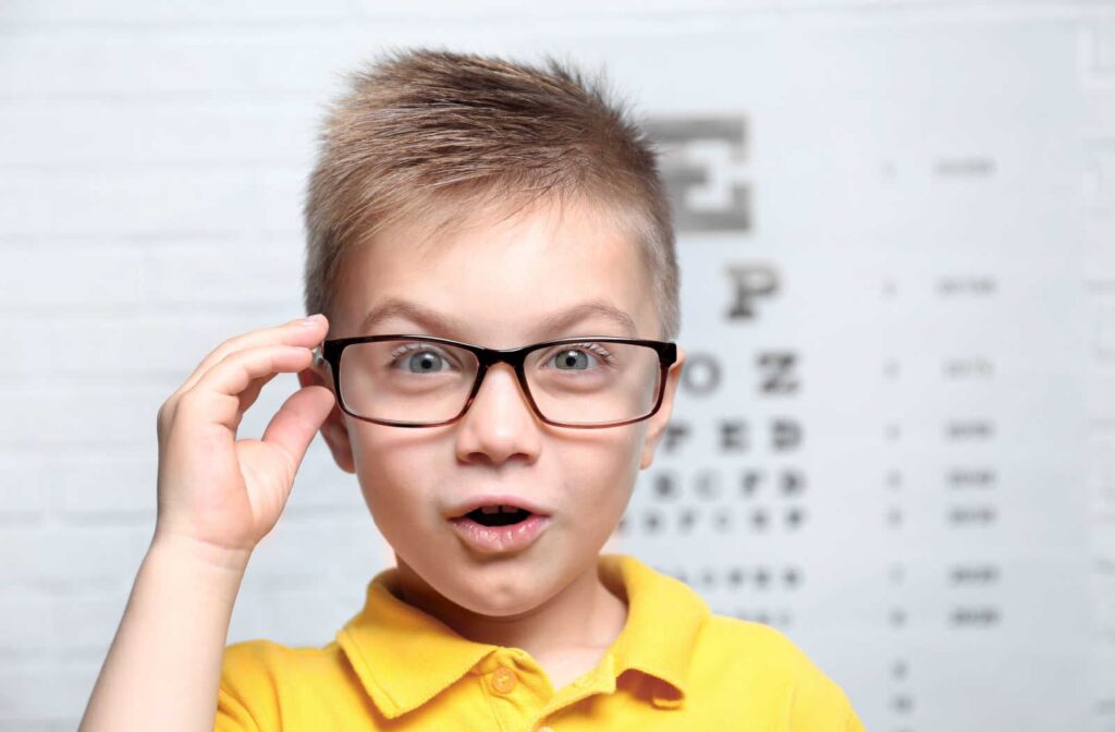 A young boy wearing glasses at the eye doctor reading an eye chart