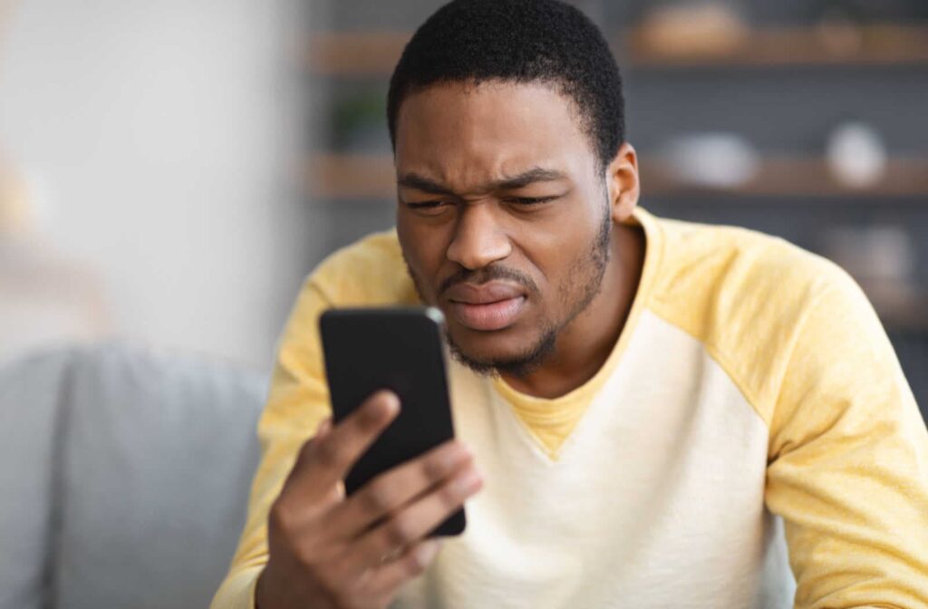 A man squinting to see his phone clearly, presenting signs of hyperopia