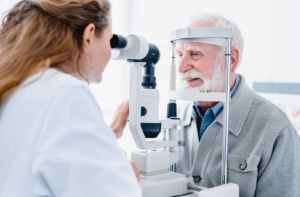 A senior man looking into an optometrist's machine and smiling as a female optometrist examines his eyes
